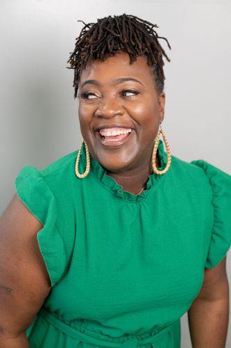 Smiling person in a bright green sleeveless top with large gold earrings against a gray background