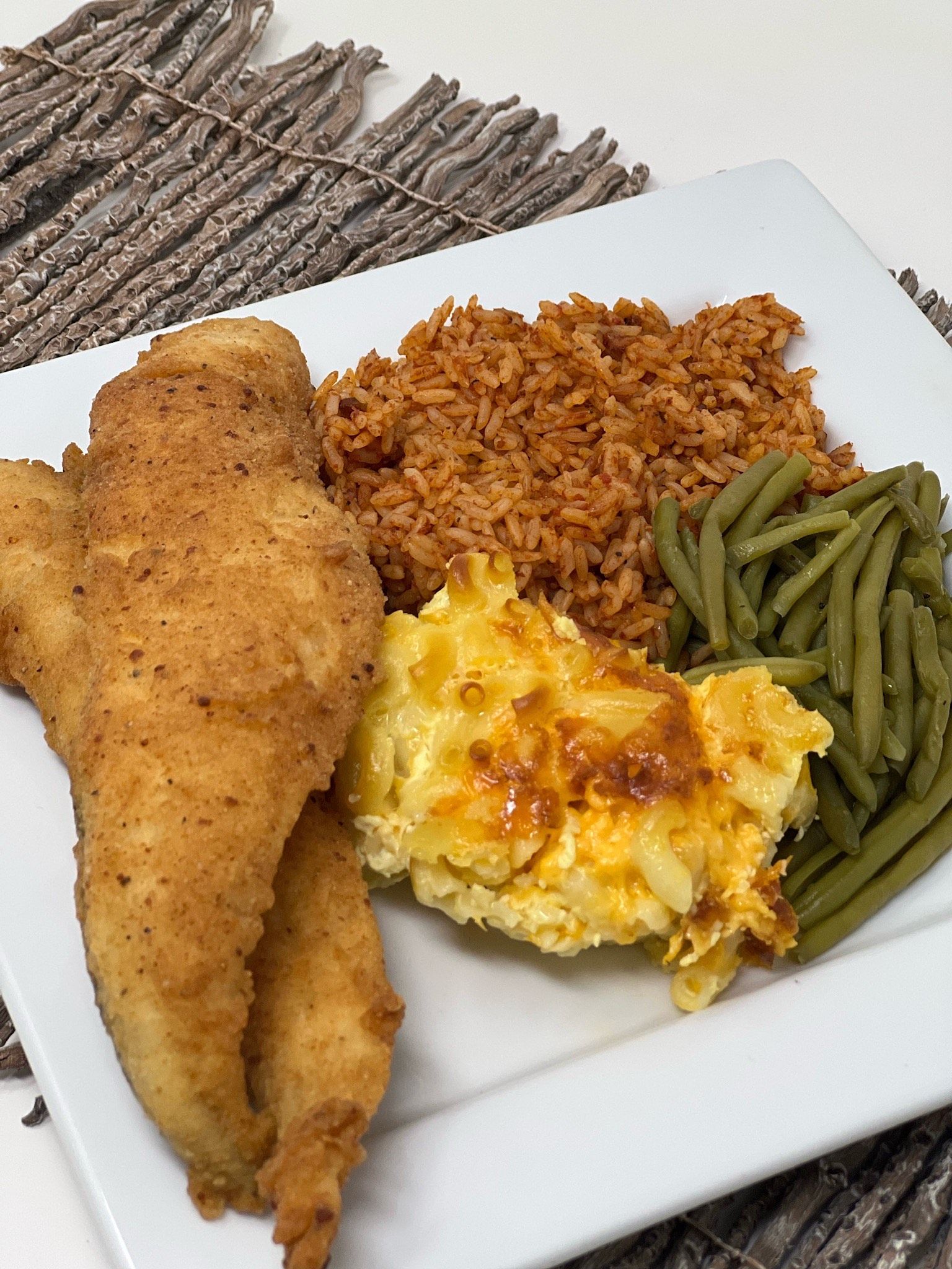 Plated meal with fried fish, rice, cheesy mashed potatoes, and green beans on a white plate