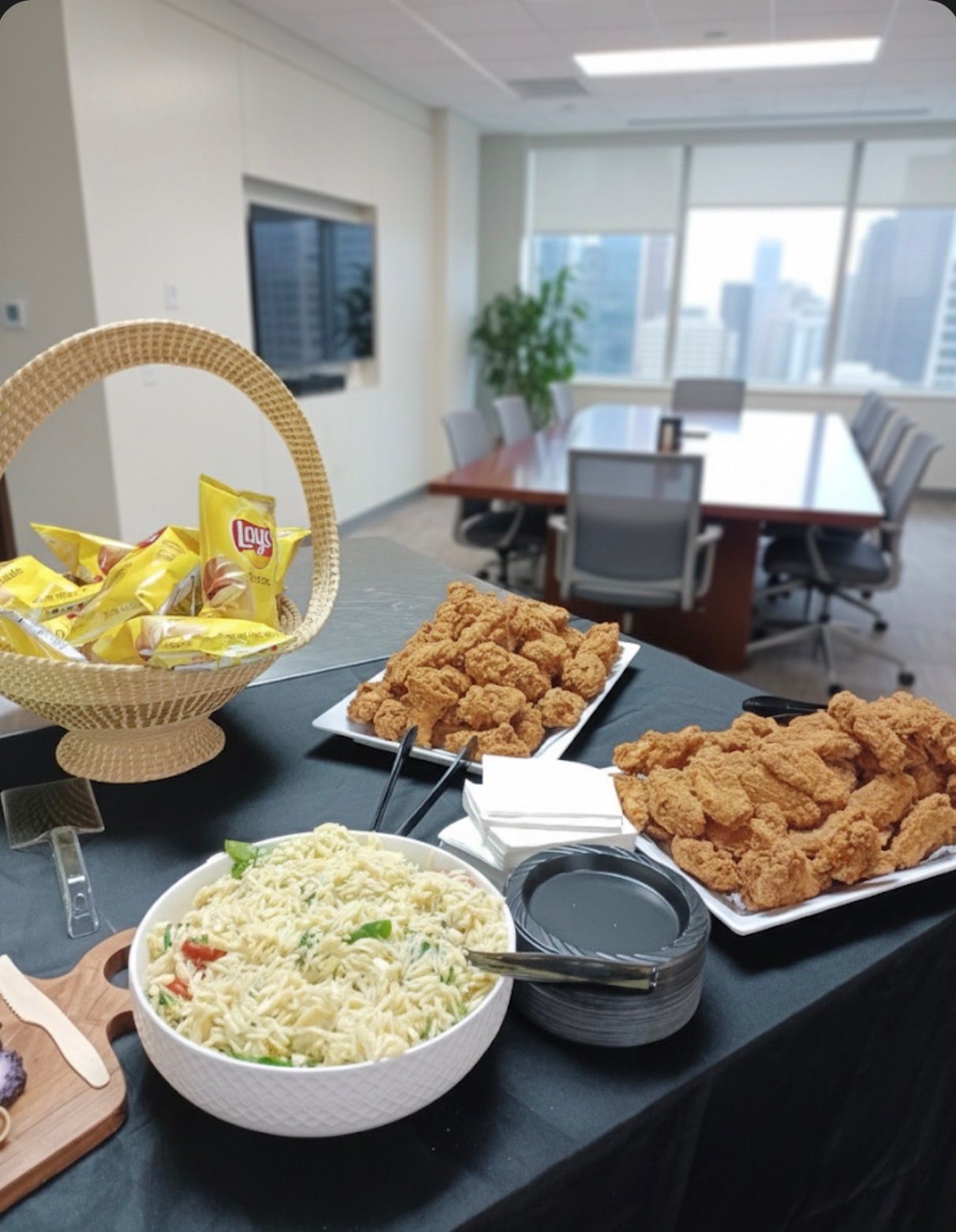 Office meeting room with buffet table of fried chicken, salad, chips, and candy basket