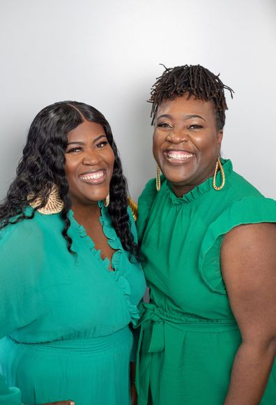 Two smiling people in green dresses posing against a white backdrop