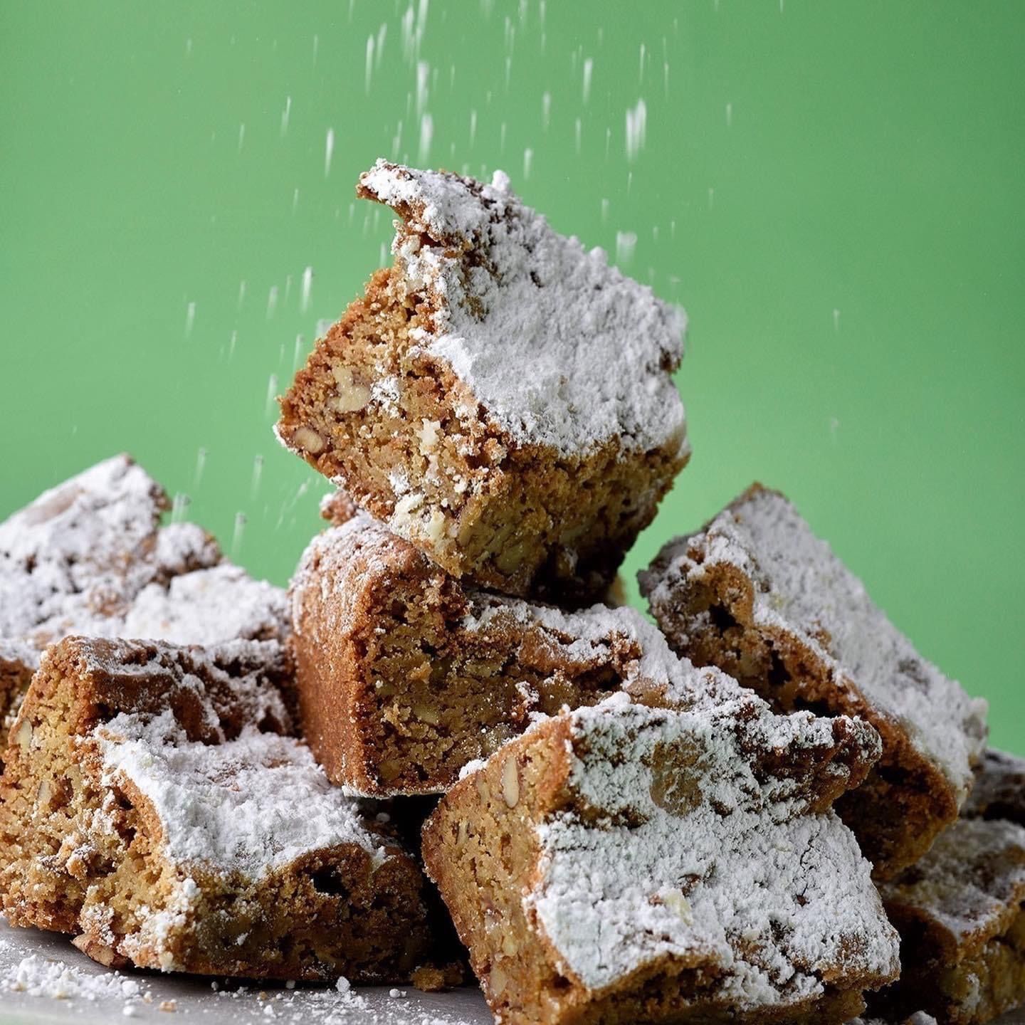 Powdered sugar-dusted brownies stacked on a plate against a green background