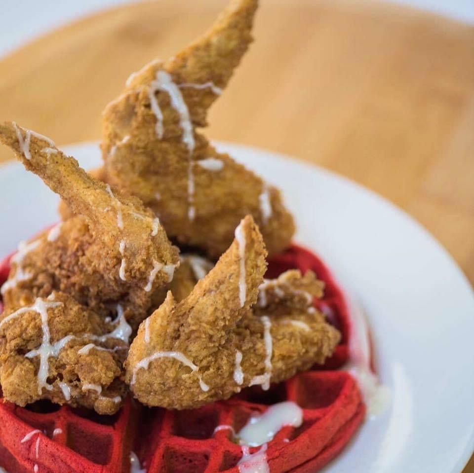 Fried chicken on a red waffle, drizzled with white sauce, on a white plate