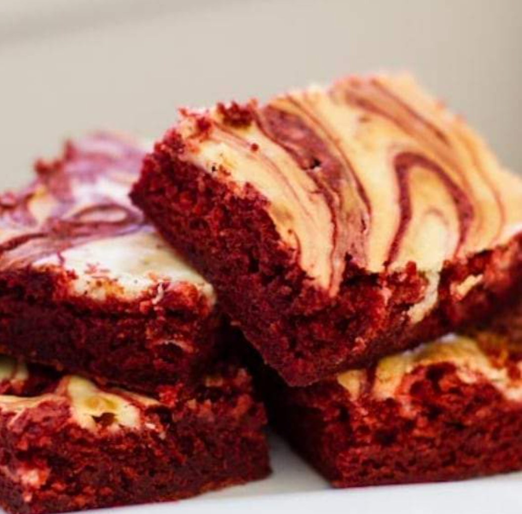 Red velvet brownies topped with swirled cream cheese frosting on a white plate