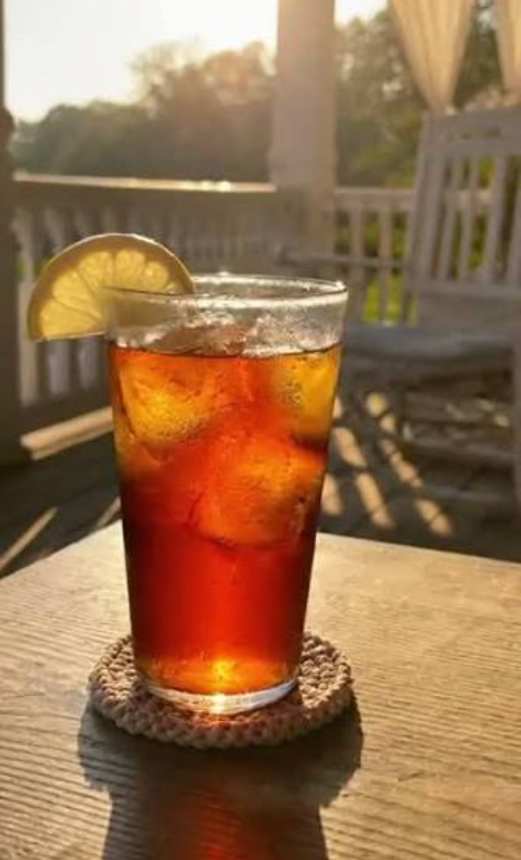 Iced tea with a lemon wedge on a coaster in warm sunlight on a patio table