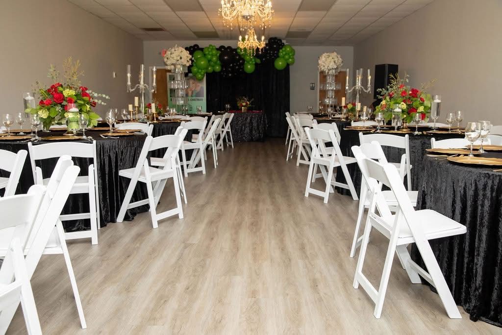 Elegant banquet hall with black-and-white table settings, white chairs, floral centerpieces, and a chandelier.