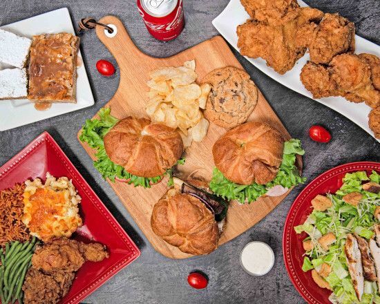 Assorted fried foods, sandwiches, salads, and a soda arranged on trays and a board.