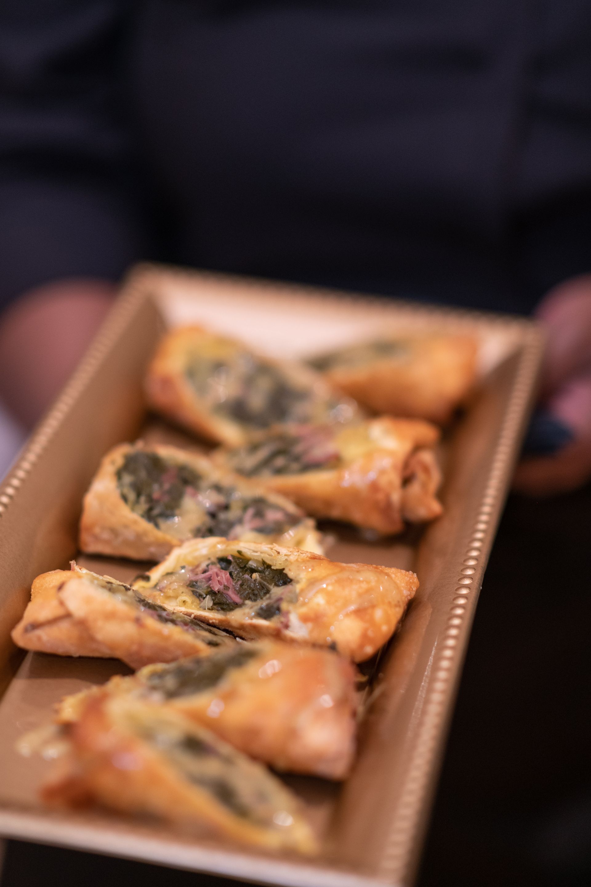 Tray of triangular fried pastries with a dark filling, held by someone in the background