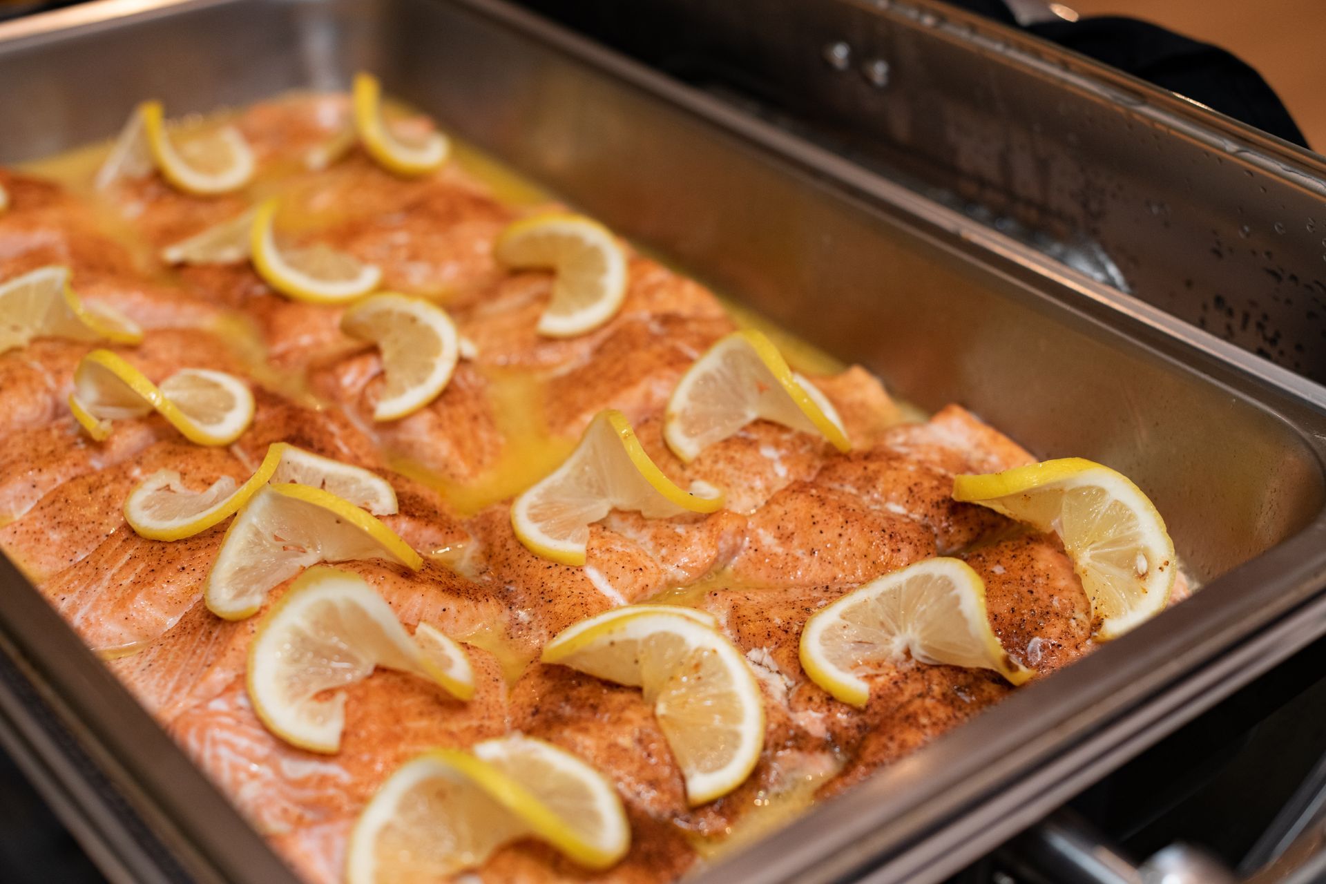 Lemon-garnished salmon fillets baking in a roasting pan in an oven