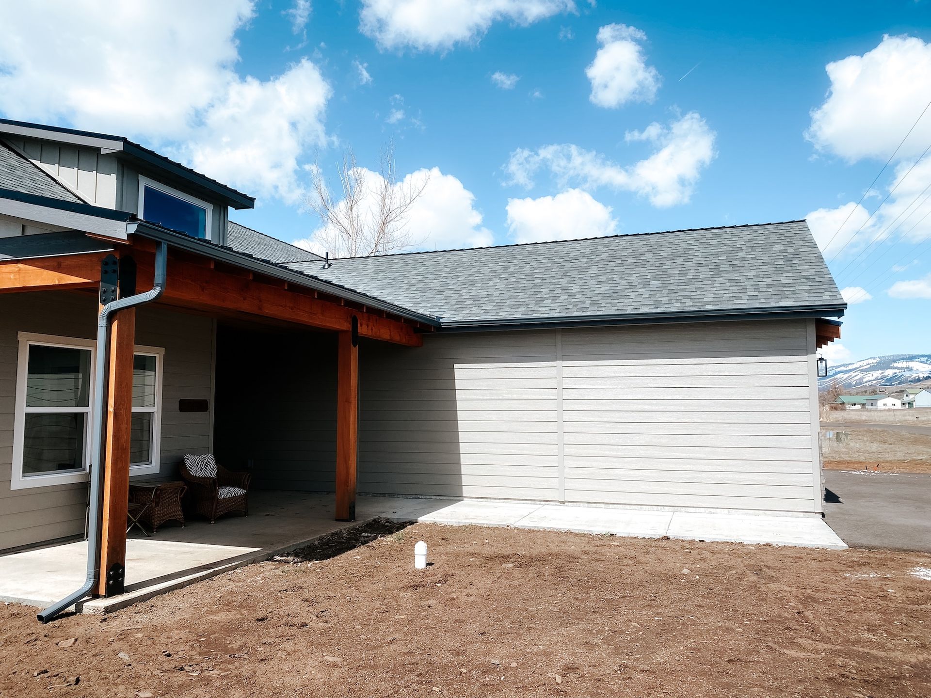Exterior of a house with a garage, white siding, and a brown dirt yard under a blue sky