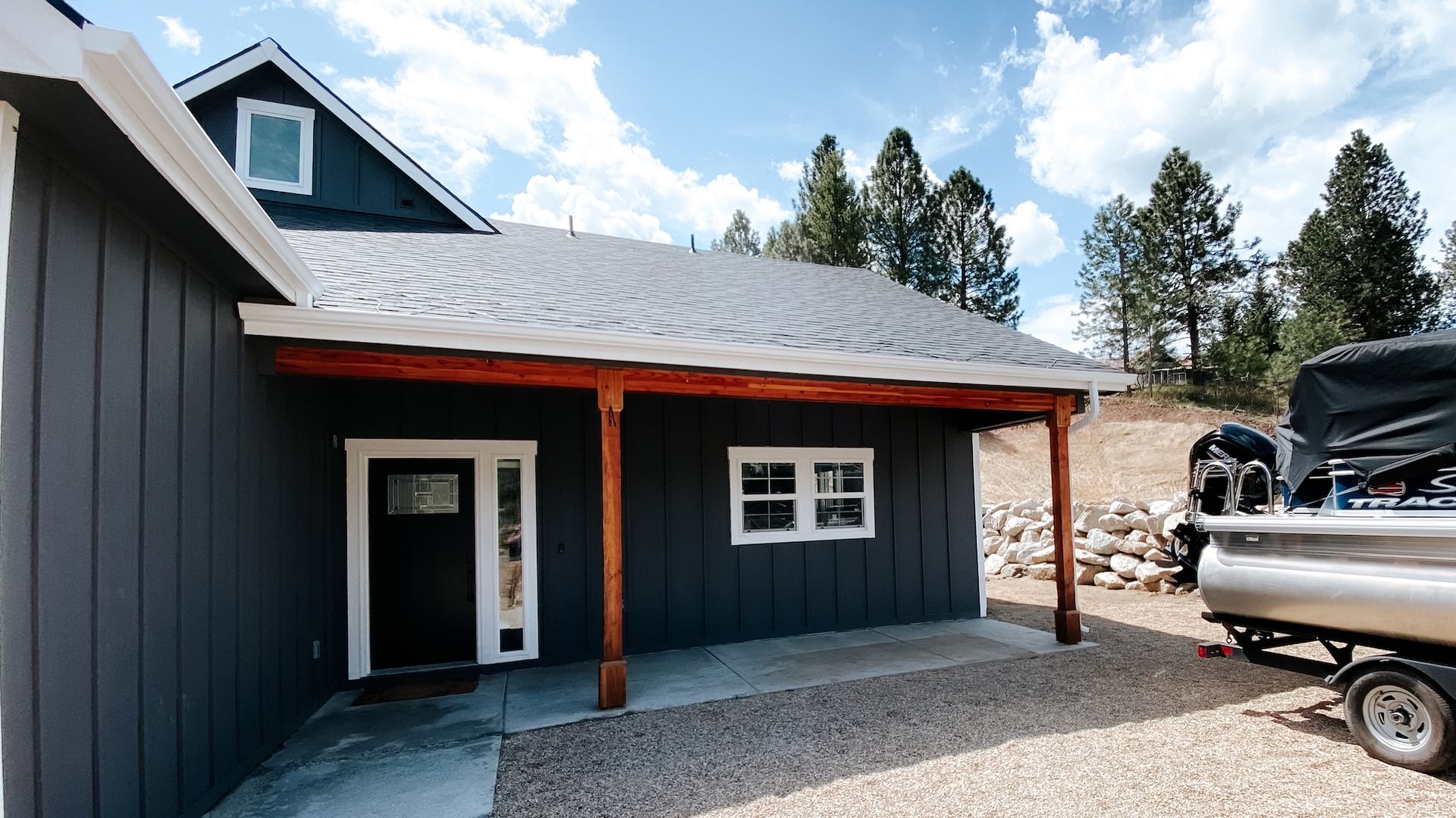 Dark blue house exterior with orange posts, gravel driveway, and a parked truck under a partly cloudy sky