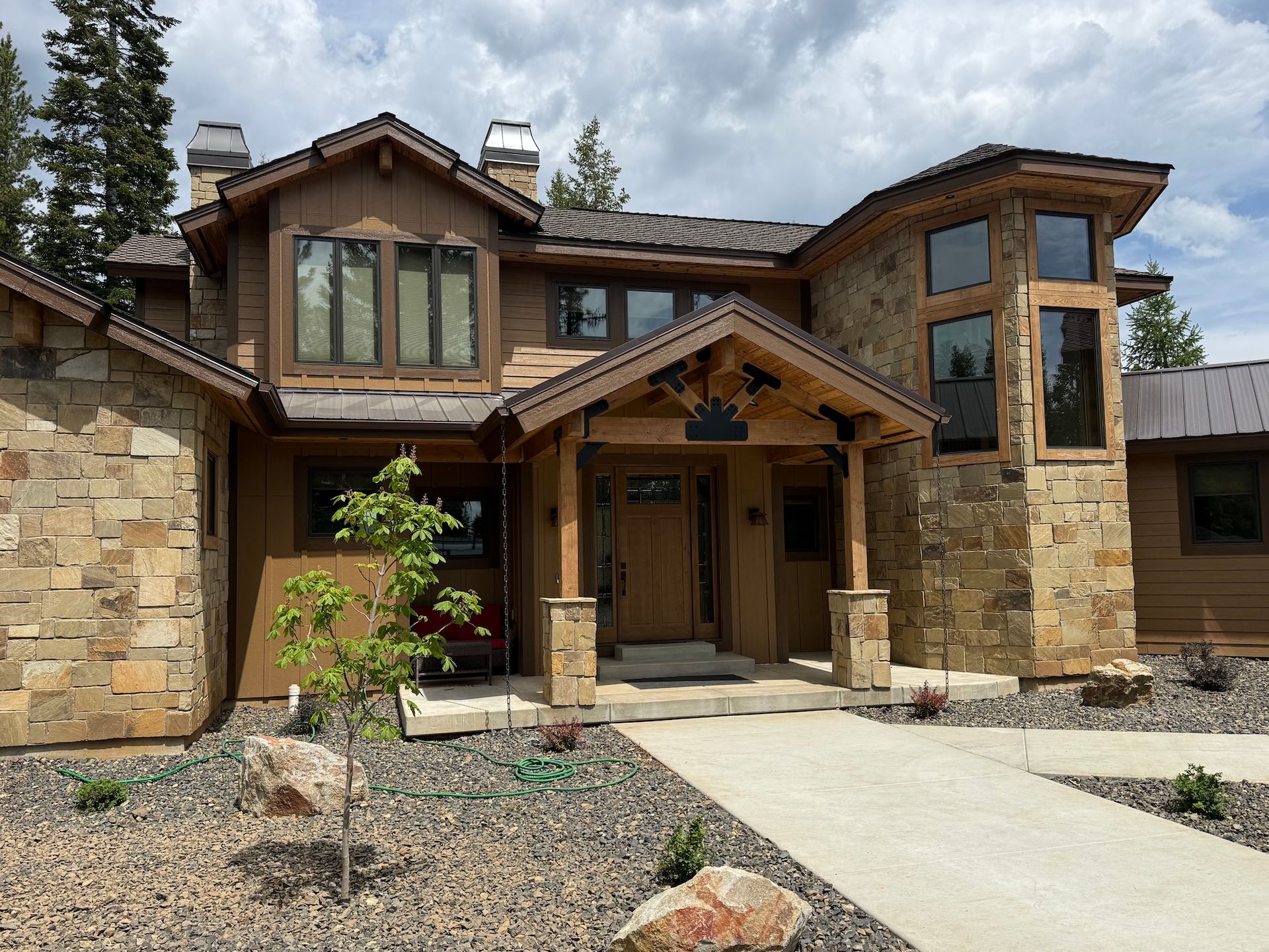 Stone-and-wood house exterior with a covered front porch and concrete walkway under a cloudy sky