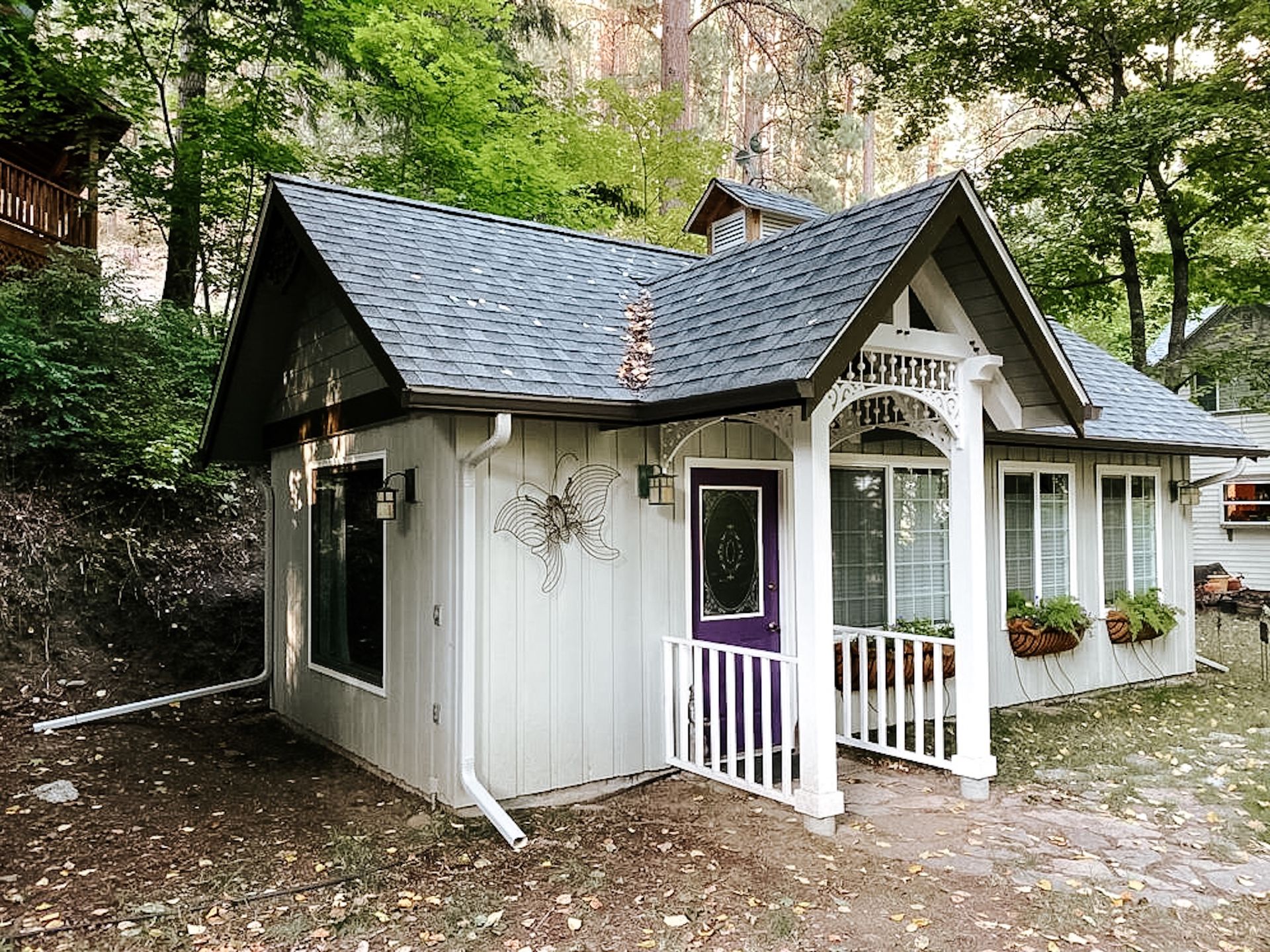 Small white cottage with dark roof and porch in a wooded setting