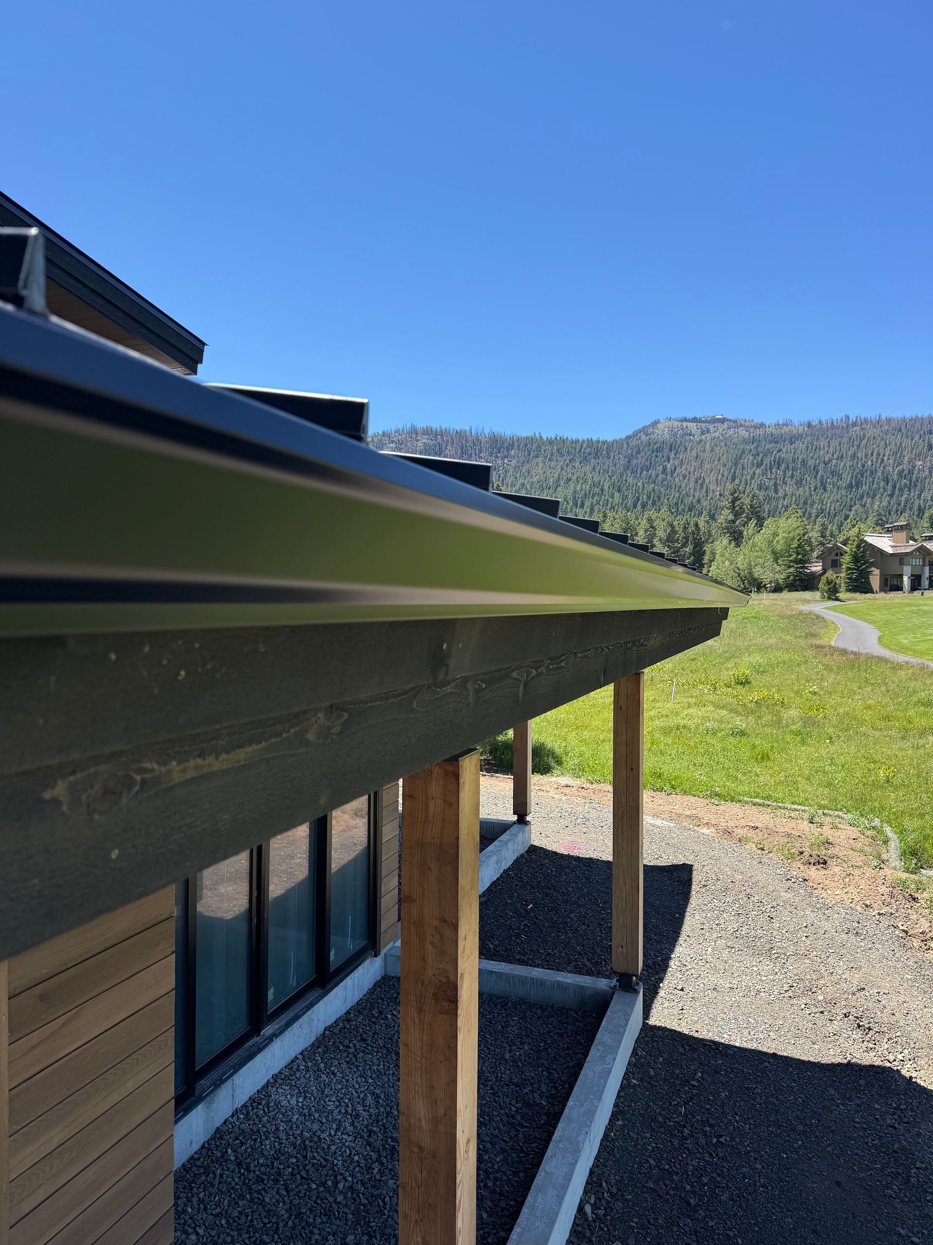 House eaves over gravel yard, with mountains and blue sky in the background.