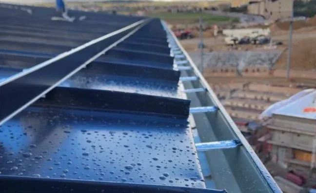 Blue metal rooftop with rain droplets, viewed along the edge at an industrial site