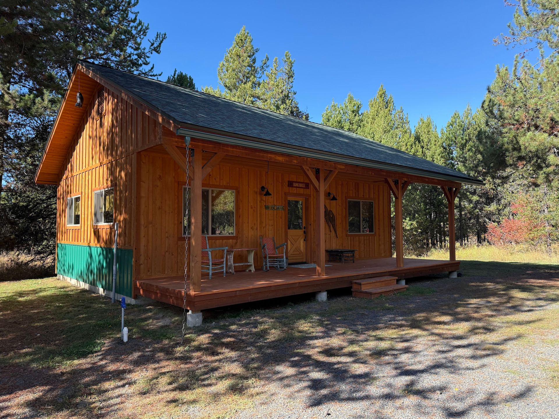 Wooden cabin with porch in a sunny forest clearing under a blue sky