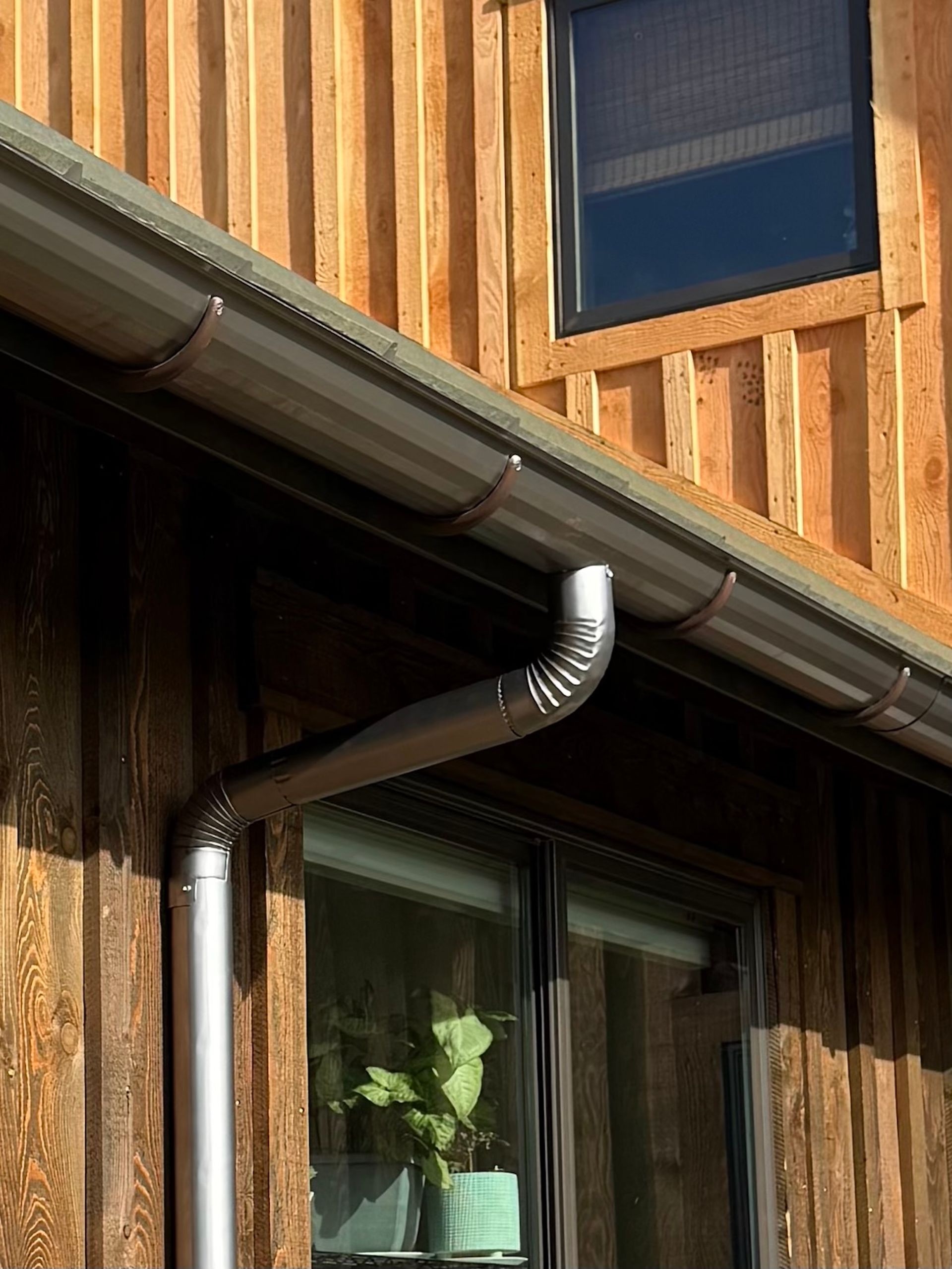 Wooden house exterior with a metal roof, downspout, and window under the eaves