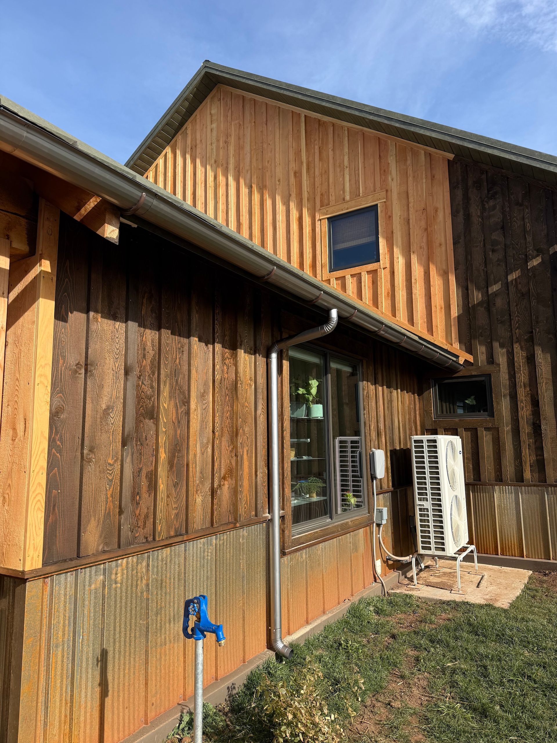 Wooden house exterior with vertical siding, a sliding glass door, and a ladder leaning beside it under a blue sky