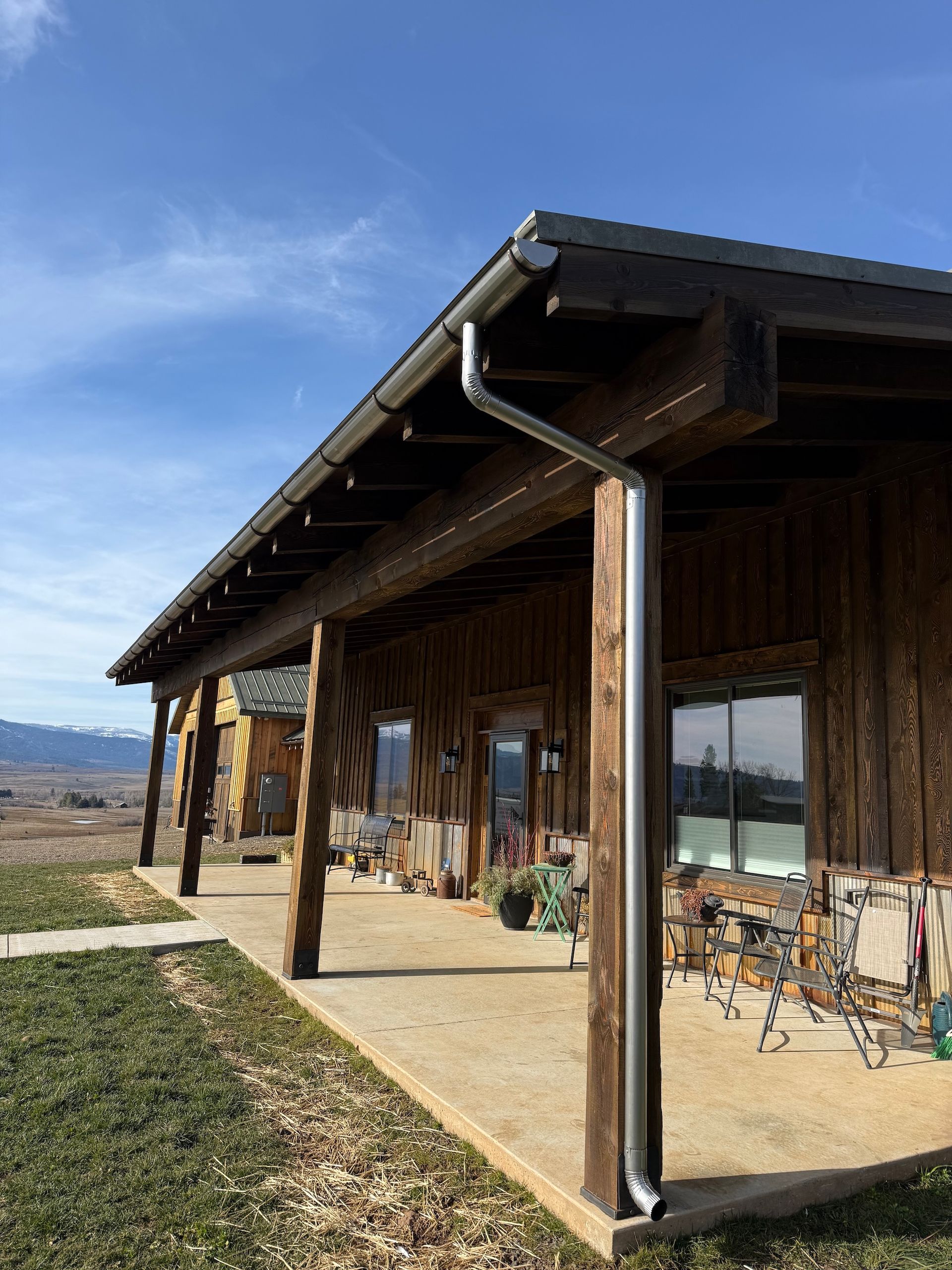 Rustic wooden porch with chairs, large windows, and a mountain view under a blue sky