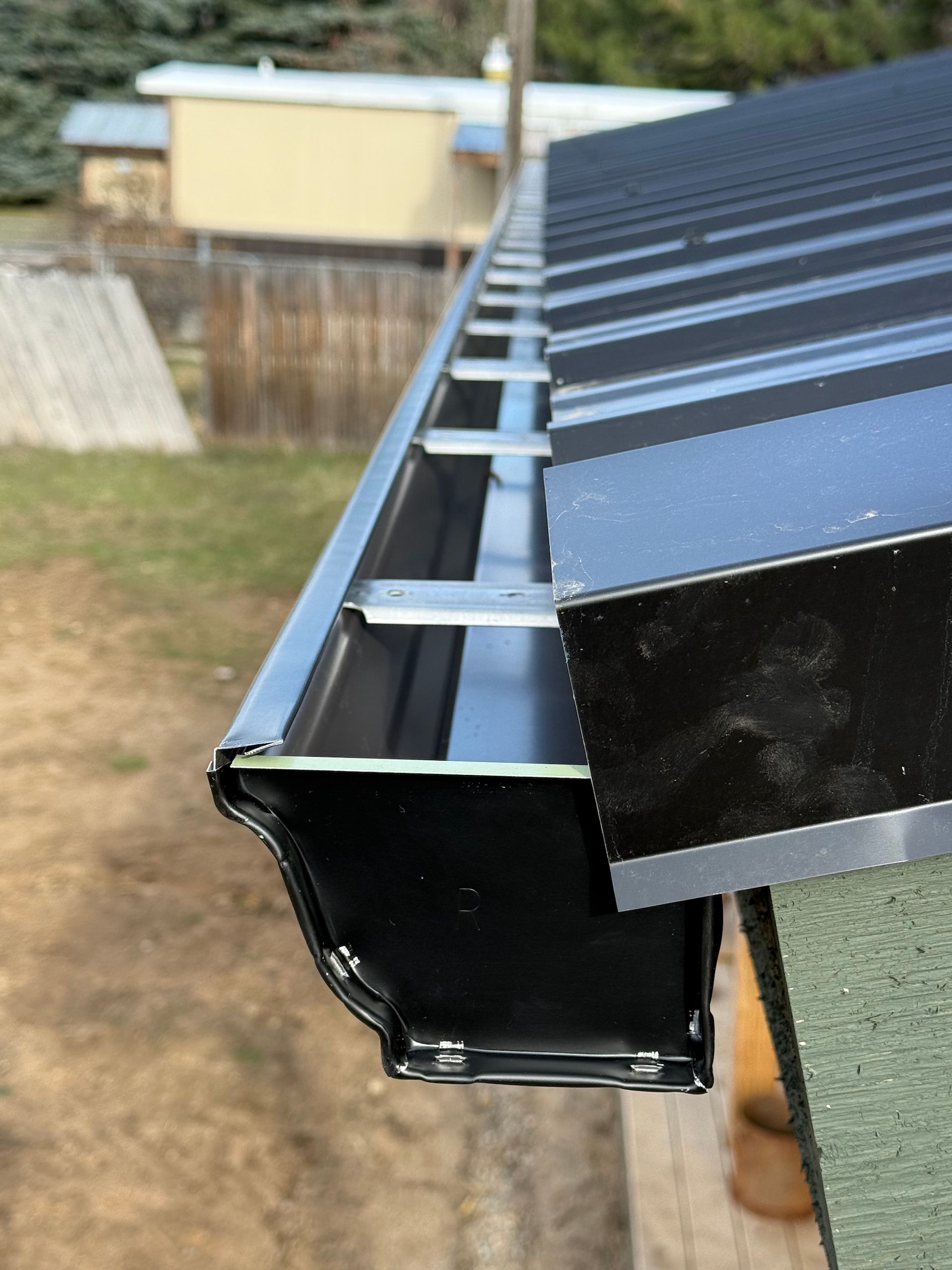 Close-up of a black metal roof gutter and fascia with exposed roof framing underneath
