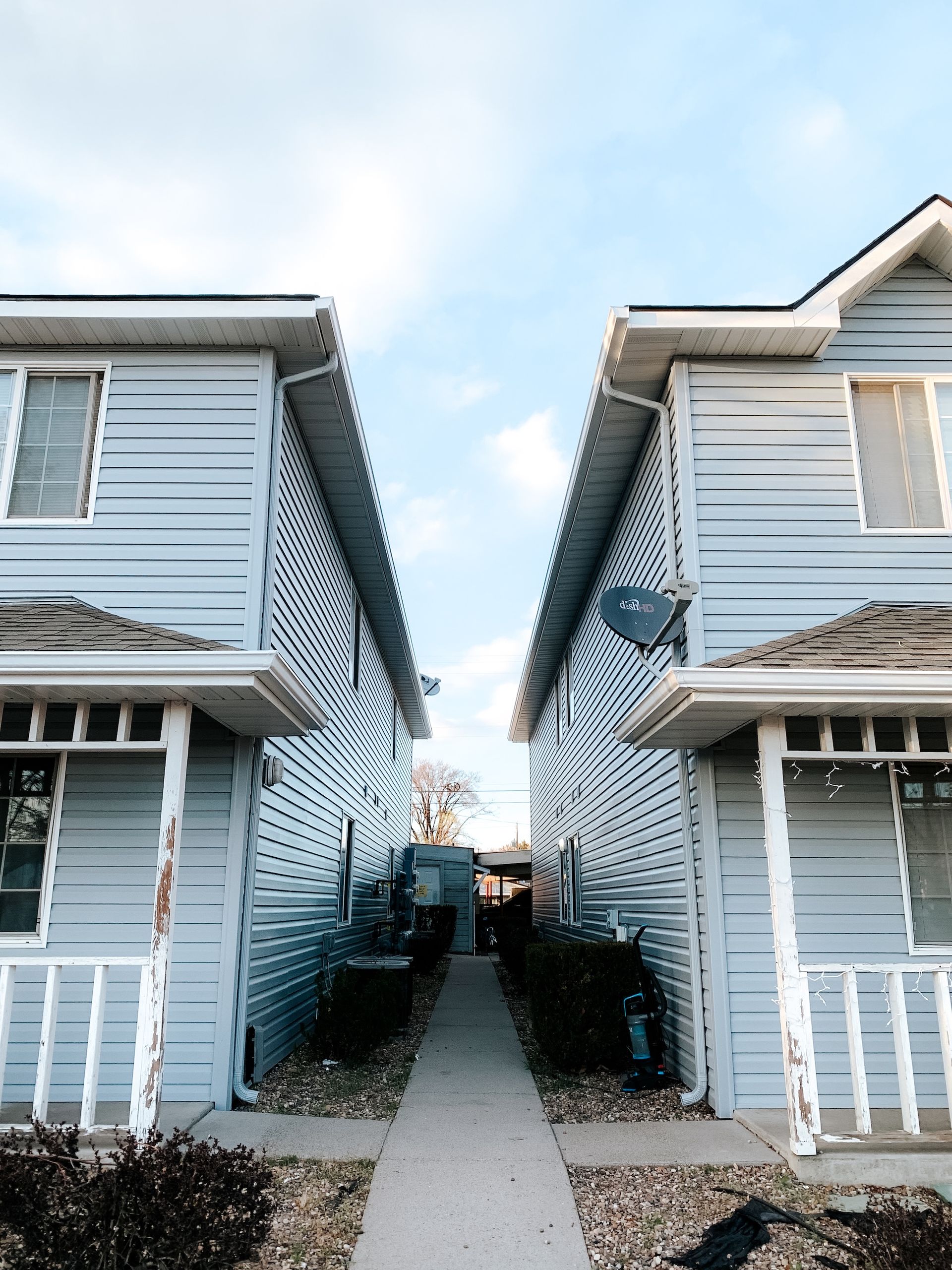 Narrow walkway between two light-blue apartment buildings under a bright sky