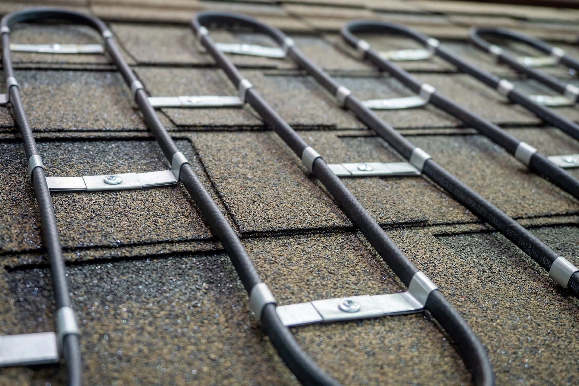 Close-up of metal cable clips securing black cords to a textured wall