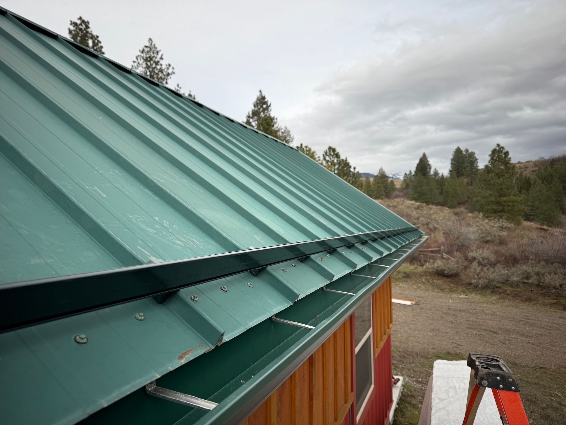 Green metal roof and gutter on a building under construction, with a wooded landscape in the background.