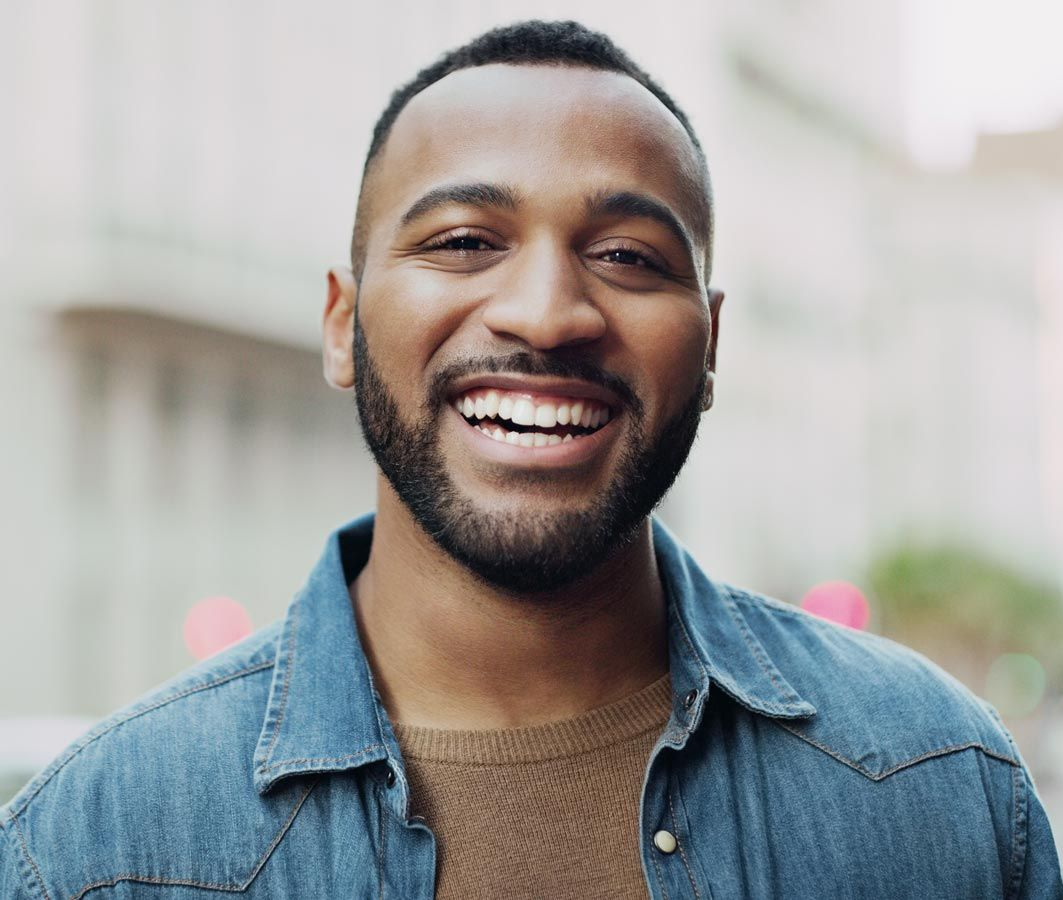 Smiling man in a denim shirt standing outdoors on a city street