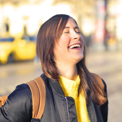 Smiling woman with backpack laughing outdoors in bright sunlight