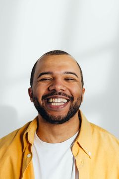 Smiling man in a yellow shirt and white T-shirt against a light background