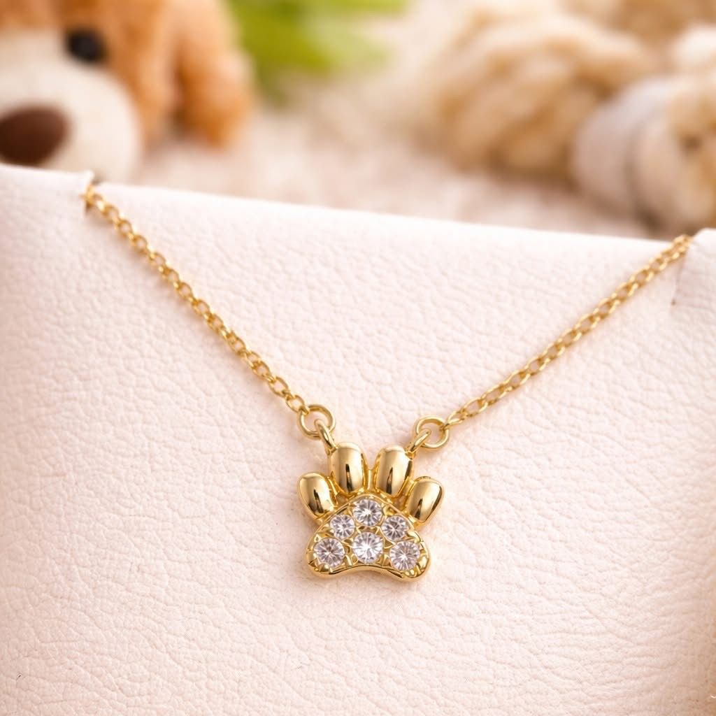 Gold paw-print pendant necklace with small clear stones on a light background