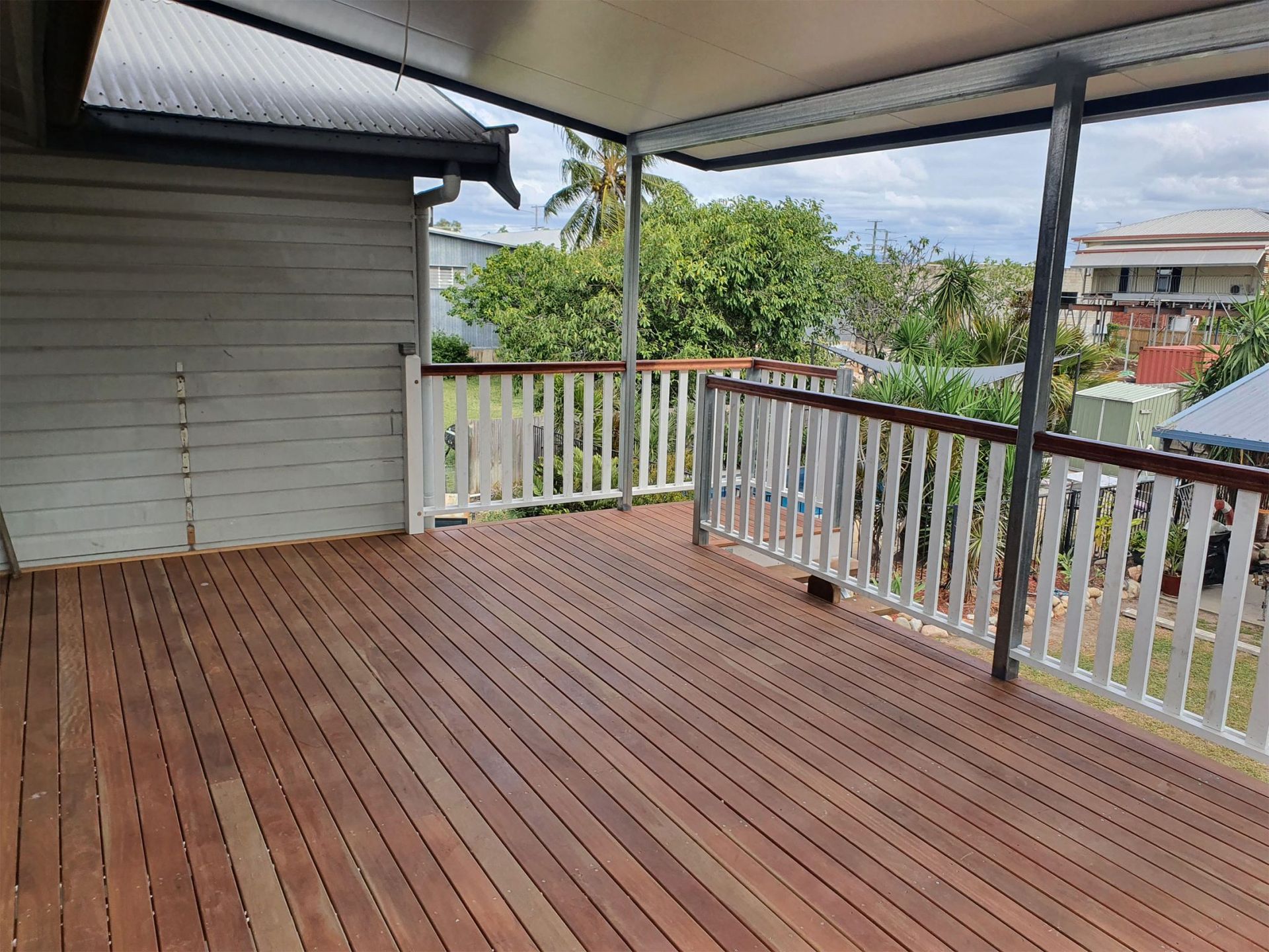 A Wooden Deck With a White Railing and a View of a House — Shane Firmin Carpentry Pty Ltd In Mount St John, QLD