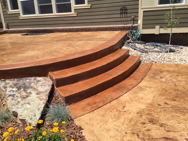 Concrete patio with steps, stamped with geometric patterns and bordered in brick red.