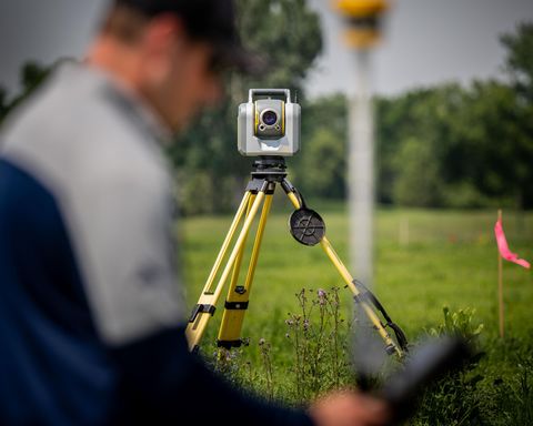 Surveyor using a total station on a tripod in a field.