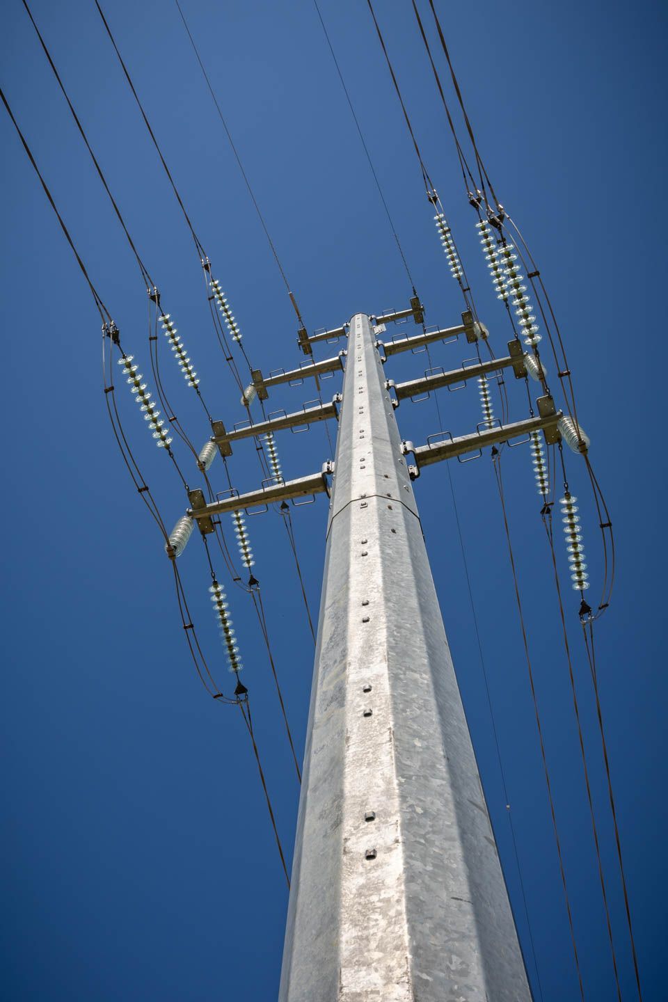 Steel power line tower against a clear blue sky, with many wires and insulators.