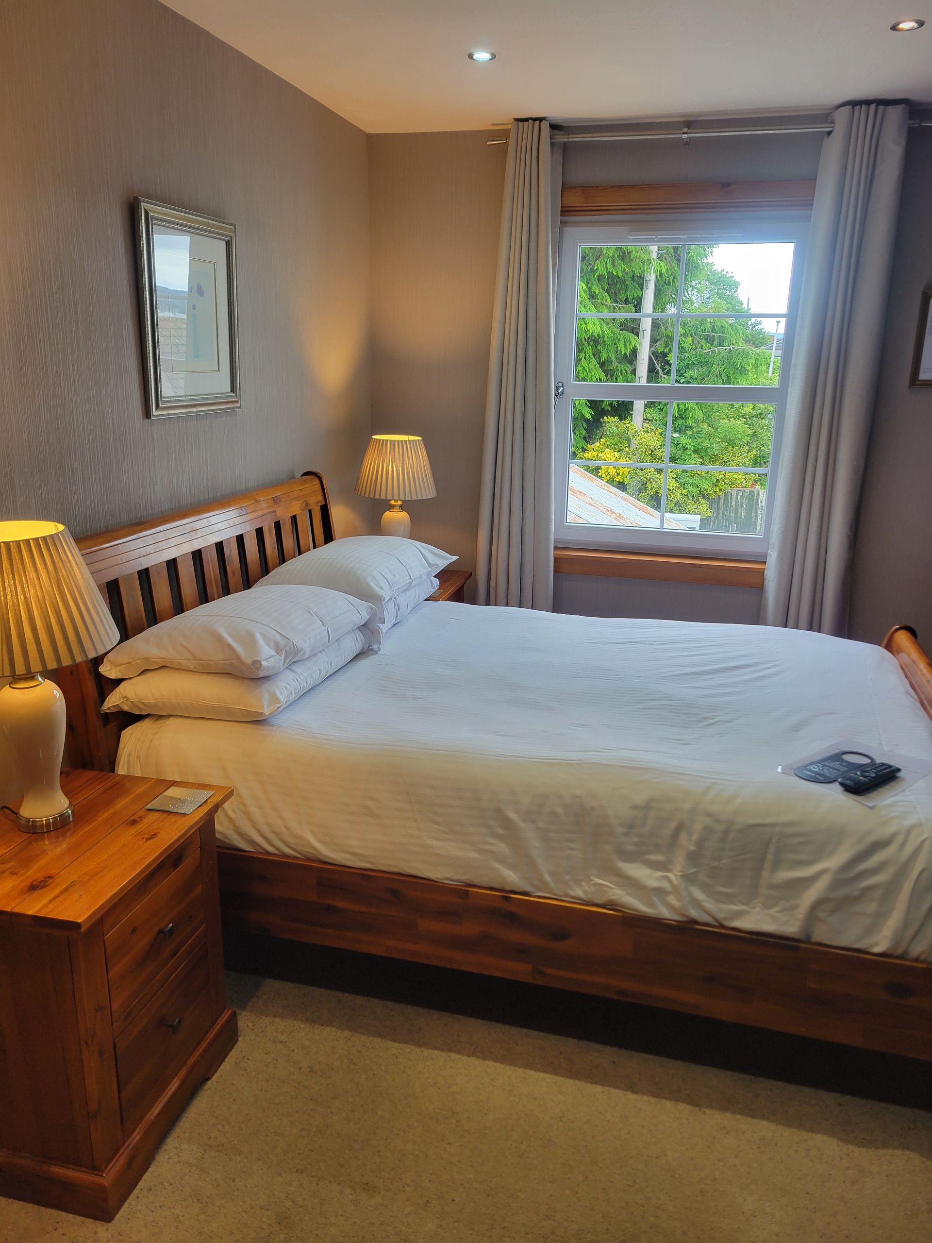 A bedroom with a bed , nightstand , mirror and window.