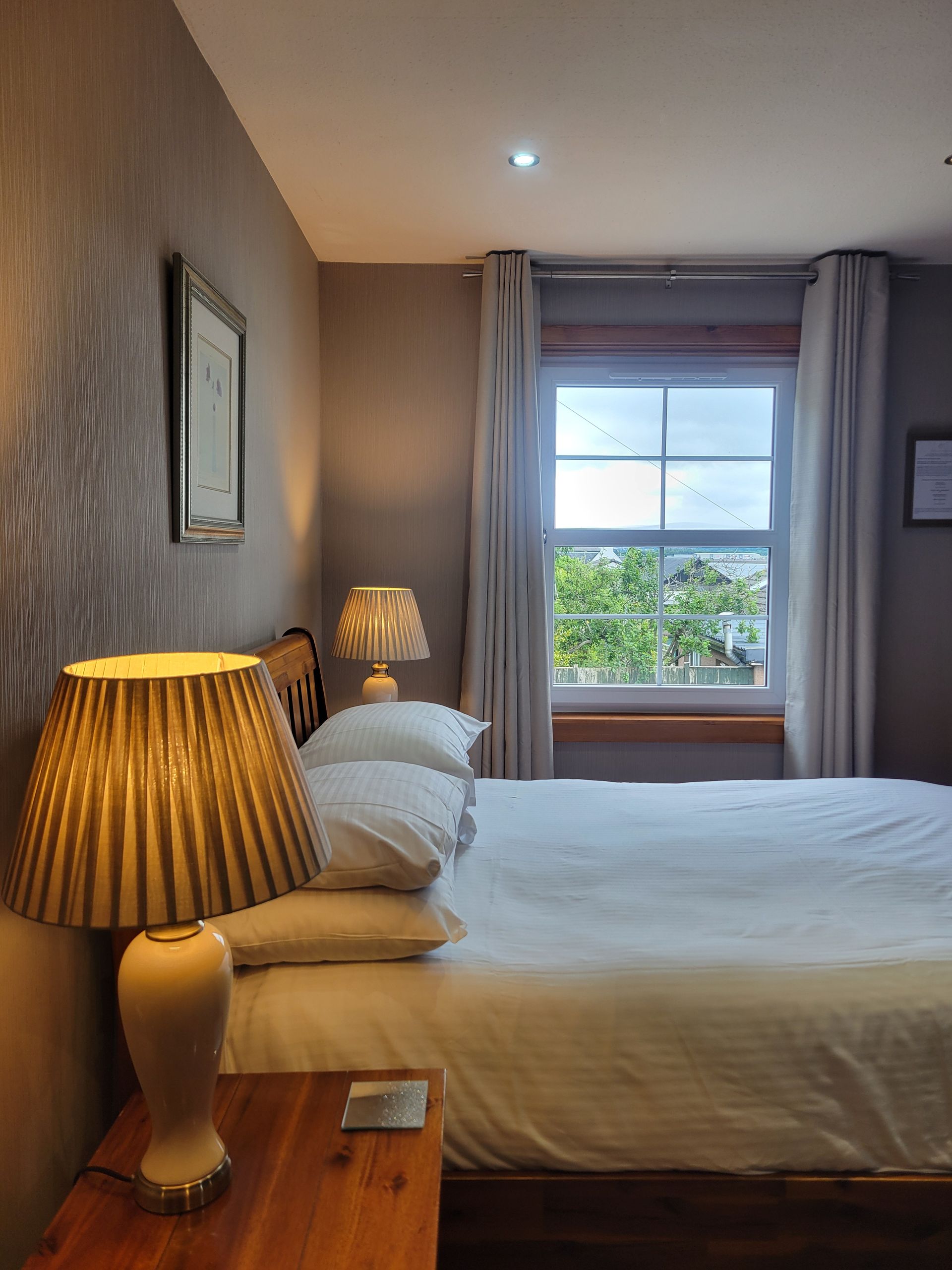 A bedroom with a bed , nightstand , mirror and window.
