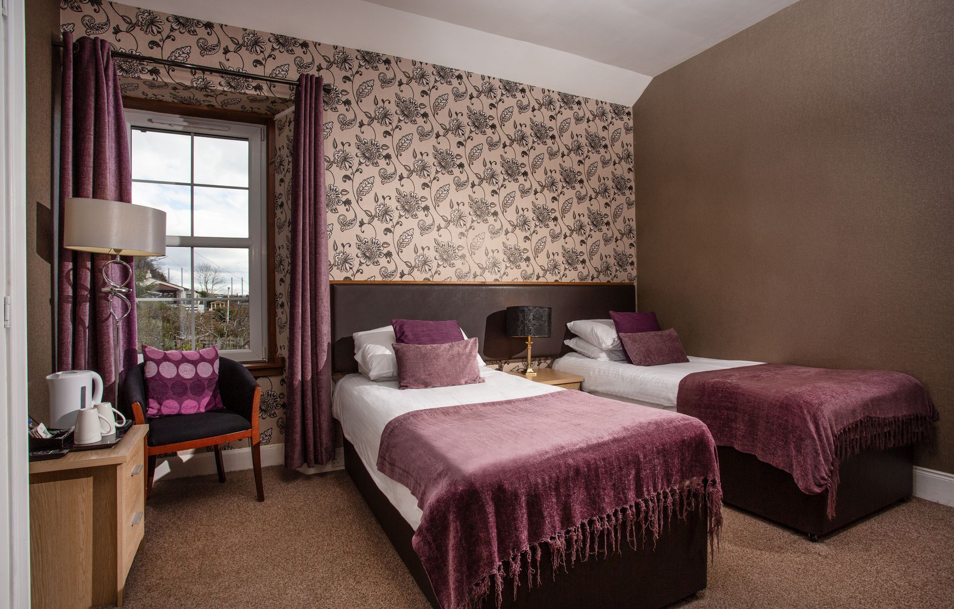 A hotel room with two beds , a chair and a window.