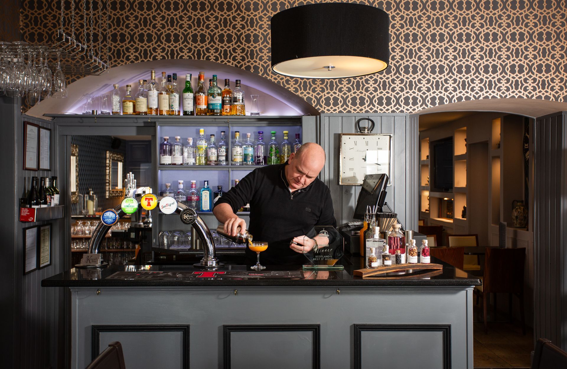 A man is pouring a drink at a bar in a restaurant.