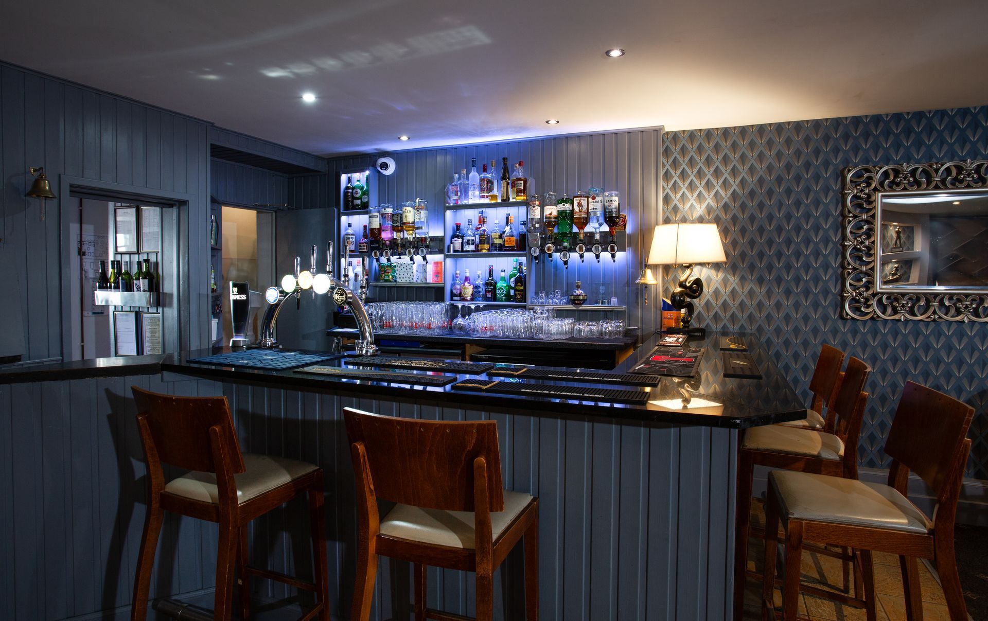 A bar with a lot of bottles on the shelves and chairs.