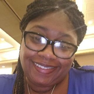 A woman wearing glasses and a blue shirt is smiling for the camera.