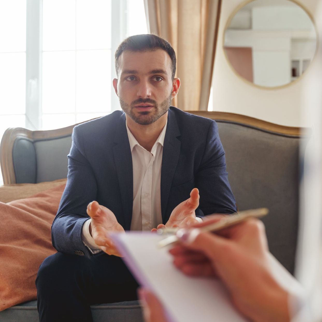 A man in a suit is sitting on a couch talking to a woman.