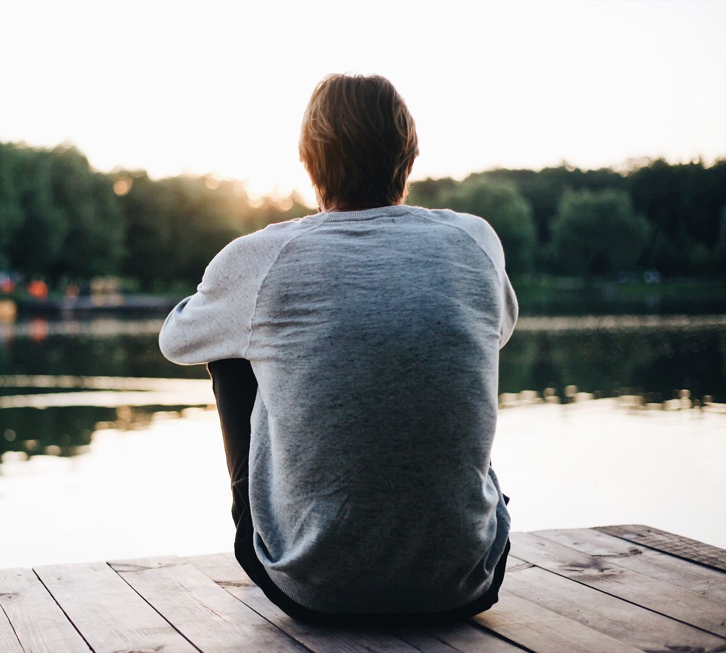 A man is sitting on a dock looking at a lake