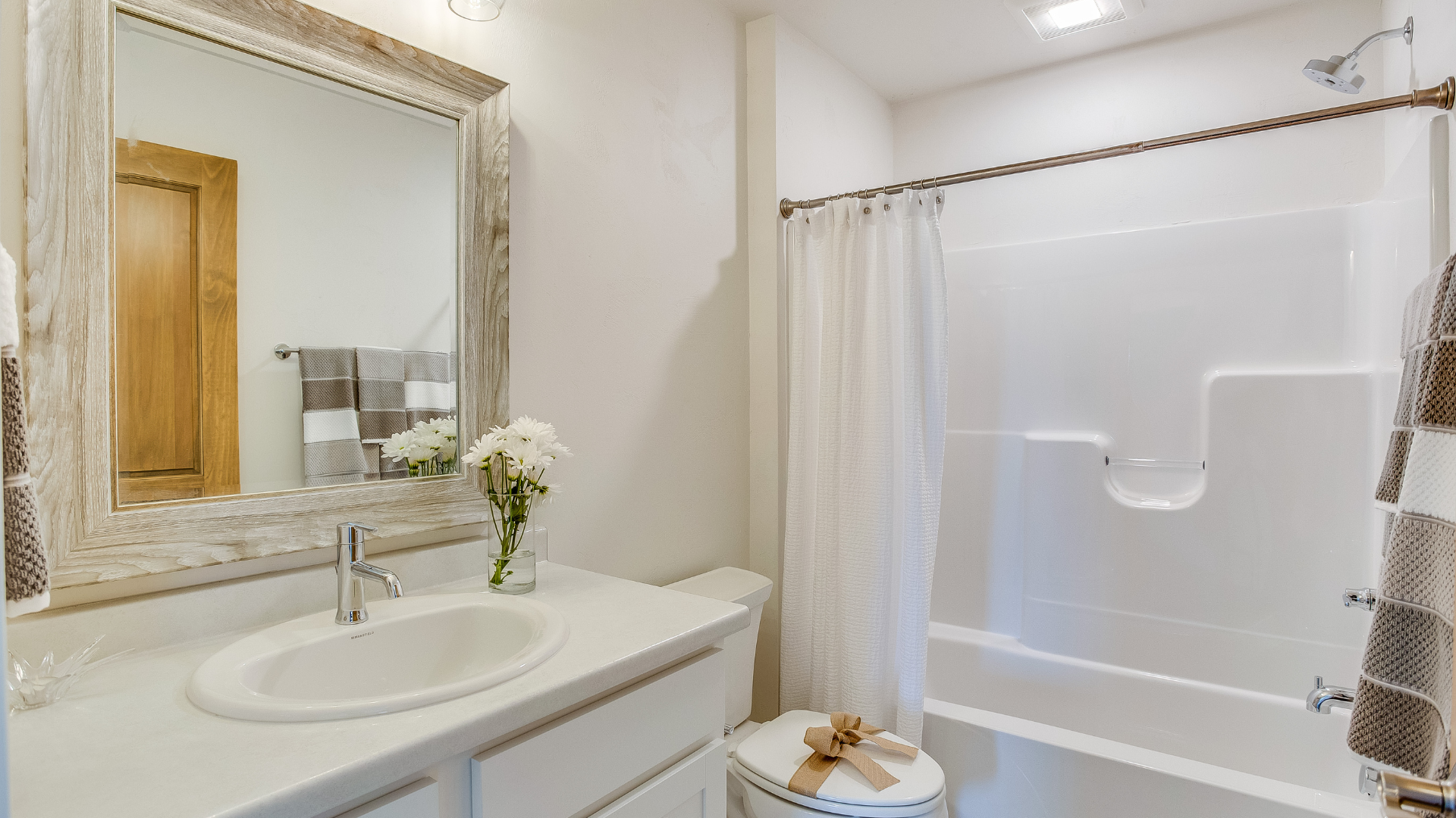 Bathroom with white walls, vanity, and shower. A floral bouquet and patterned towels are visible.