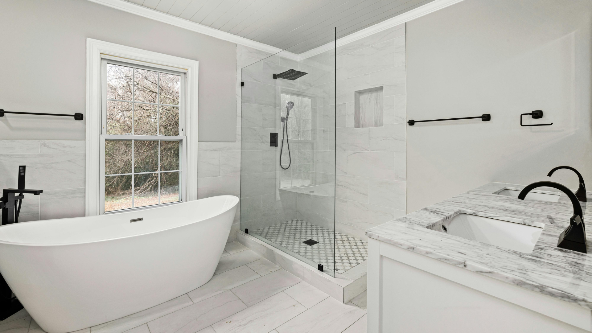 Modern bathroom with white tub, shower, vanity, and marble tile; black fixtures.