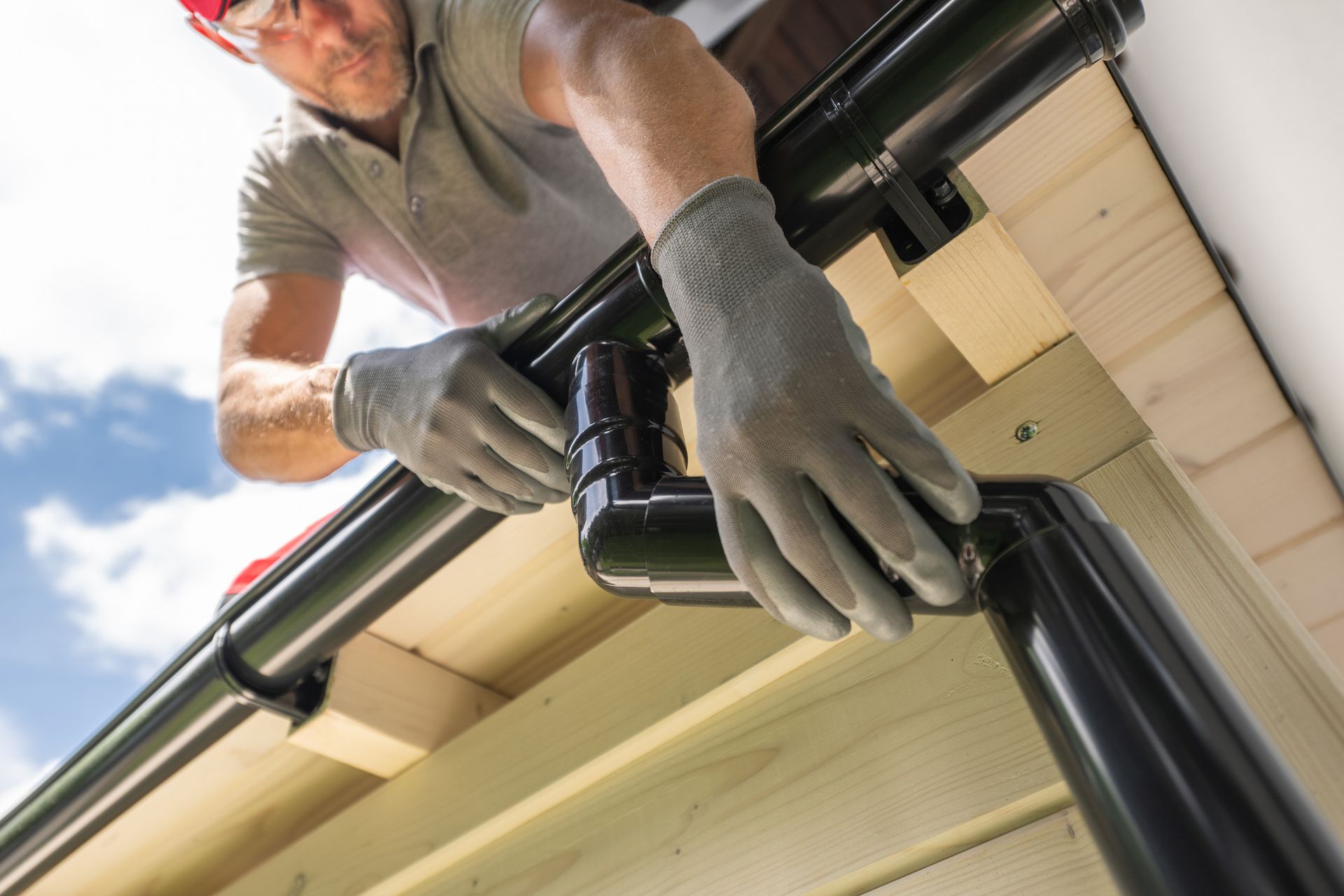 Image of a worker installing a black gutter on a wooden structure.