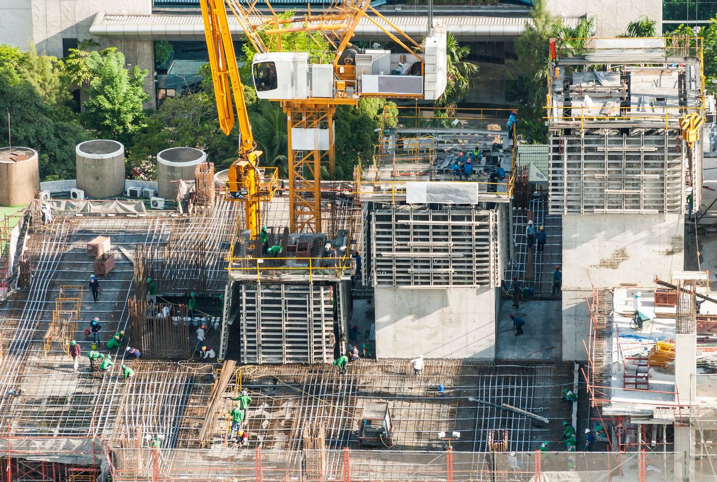 Cantiere edile con edifici in cemento e alte gru sotto un cielo azzurro e limpido.