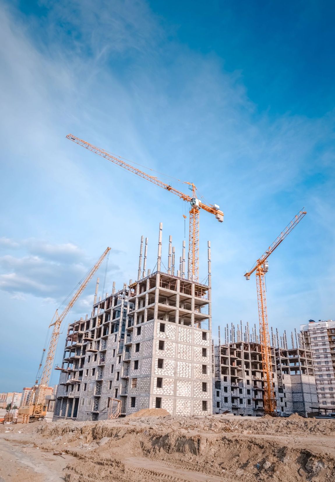 Cantiere edile con edifici in cemento e alte gru sotto un cielo azzurro e limpido.