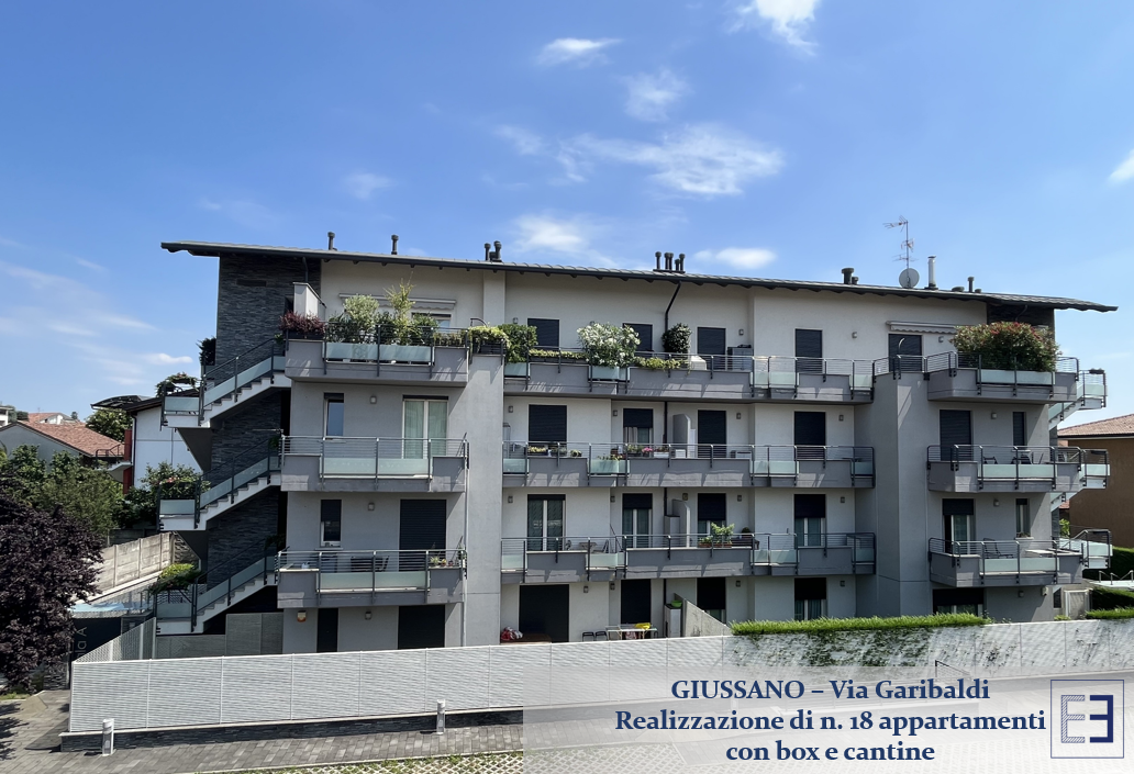 Palazzo di appartamenti con balconi e piante in vaso dietro una recinzione bianca sotto un cielo azzurro