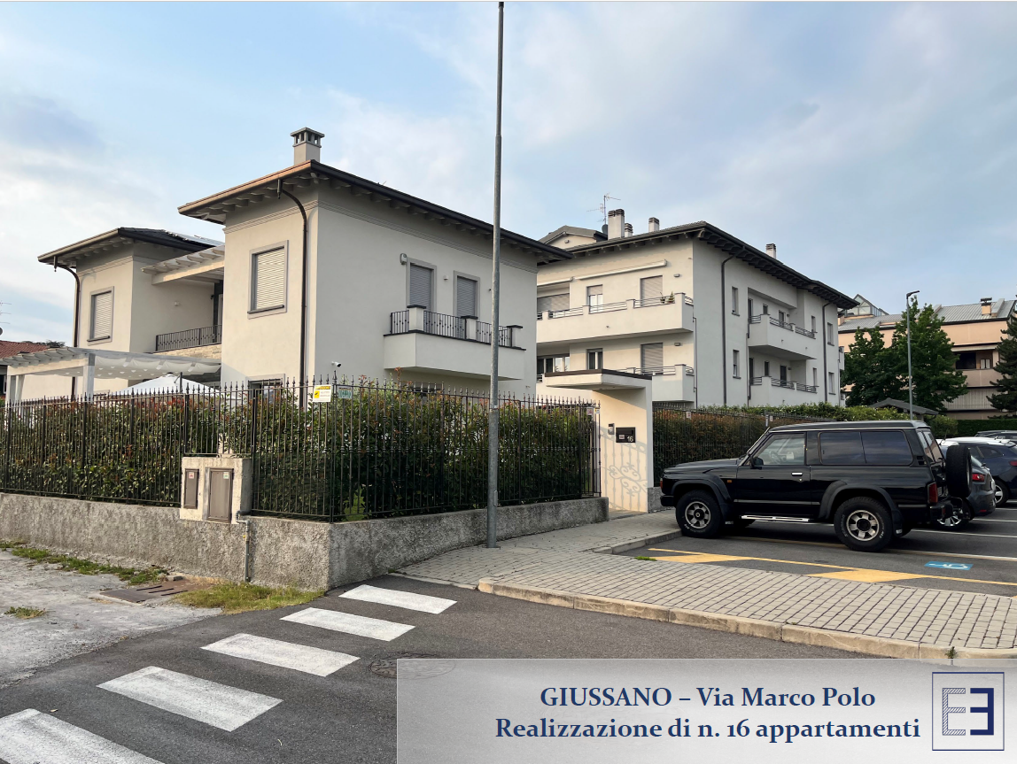 Angolo di strada con una casa beige, un SUV nero parcheggiato e un attraversamento pedonale a Giussano, Italia.