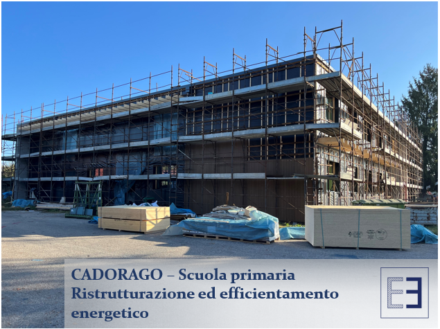 School building under renovation with scaffolding and a sign reading “Cadorago - Scuola primaria ristrutturazione ed efficientamento energetico”